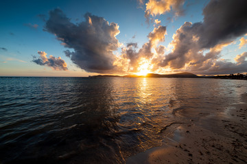 Dark clouds and shining sun over Alghero shore at sunset