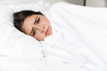 Upset lovely young girl wearing pajamas laying in bed