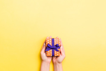 Woman arms holding gift box with colored ribbon on yellow table background, top view and copy space for you design
