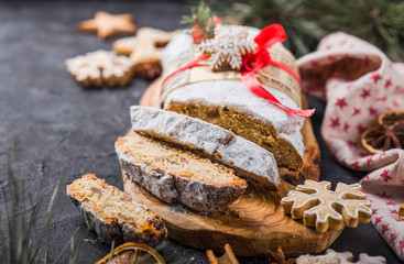 Stollen. sliced homemade Christmas dessert stollen with dried berries and nuts on stone  rustic table with cinnamon, orange slices, Christmas tree branches, gingerbread , selective focus
