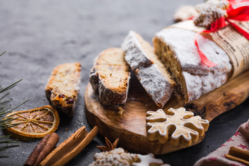 Stollen. sliced homemade Christmas dessert stollen with dried berries and nuts on stone  rustic table with cinnamon, orange slices, Christmas tree branches, gingerbread , selective focus