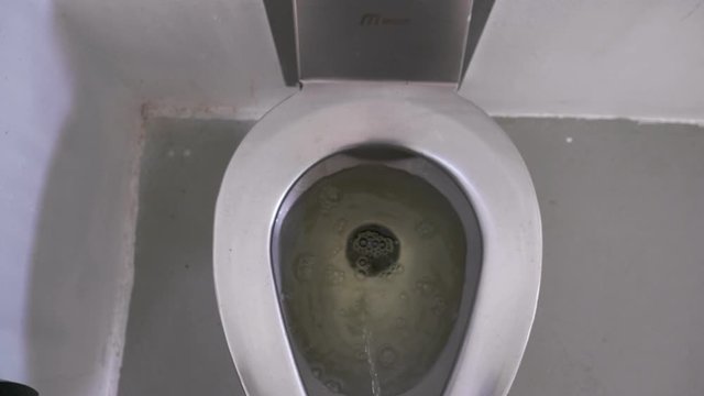 Male urinating in a public restroom. Stainless steel toilet. Handheld.