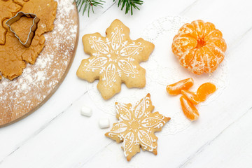 Fototapeta na wymiar Christmas gingerbread snowflakes lie on a white wooden background. tangerine, marshmallows, gingerbread dough and natural spruce on the background. view from above