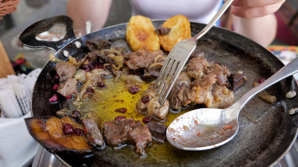 Traditional azerbaijan cuisine food in the restaurant. Woman is eating meat with vegetables served in frying pan, hands closeup. . Traditional eastern food.