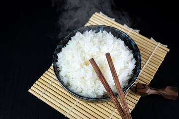 Cooked jasmine rice in ceramic cups and chopsticks Placed on a black wooden table. Close up shot. 45 degree angle.