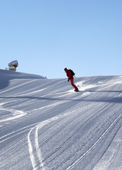 Snowboarder descends on snowy ski slope prepared by snowcat