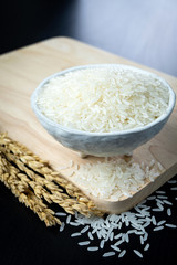 Jasmine rice in ceramic cups and ear of rice on a black wooden table. 45 degree angle.