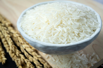 Jasmine rice in ceramic cups and ear of rice on a black wooden table. Close up shot. 45 degree angle.