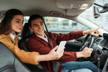 Woman passenger looking at smartphone while taxi driver pointing on road