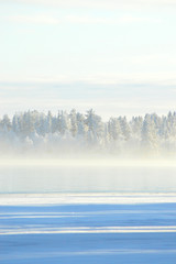 Finnish winter. Crystal clear cold winter day. Lake Porontima, Kuusamo. Bright colors and snowy forest on backround.Mist on the lake and pastel color cloudletts.