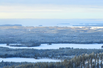 Finnisht winter, Kuusamo. Landscape from Konttainen. Fading daylight, colorful horizon and frozen lakes. Mist descends over the forested hills.