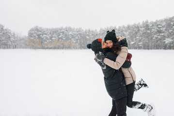 Fototapeta na wymiar Happy couple are walking in the snowy forest. The guy lifted the girl in his arms and they laugh
