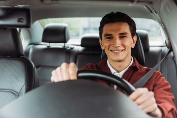 Smiling handsome man holding steering wheel of car