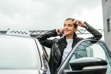 Smiling woman taxi driver talking on smartphone beside car