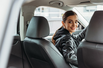 Smiling woman taxi driver looking at passenger seat of auto