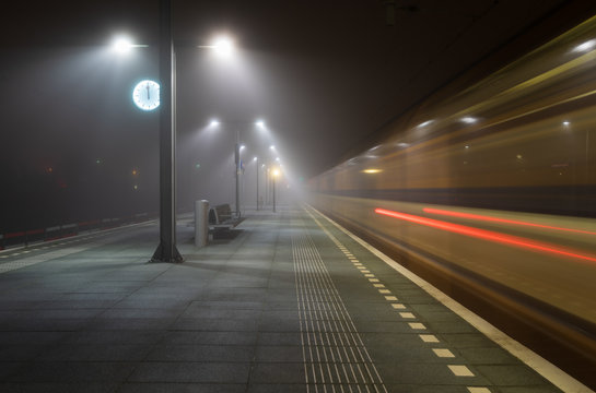 Train passing an empty platform at a railroad station during a foggy evening. Groningen, Holland.