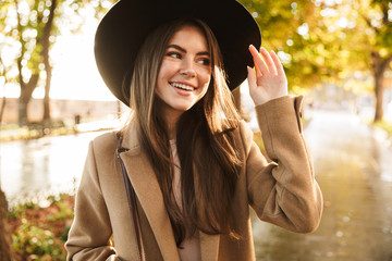 Portrait of positive woman wearing coat and hat walking in autumn park