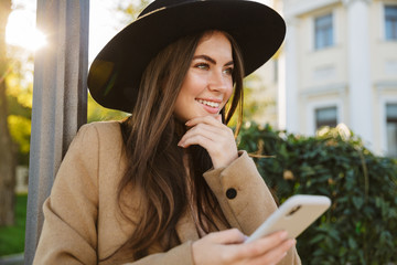 Portrait of pleased woman holding smartphone while walking outdoors