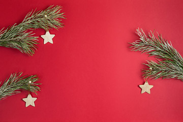 A Christmas toy wooden homemade in the form of a stars hanging on a pine branchs with hoarfrost. Flat lay on red background with copy space in the center.