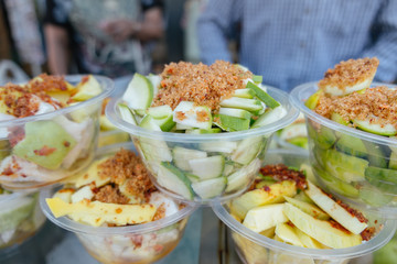 Fresh peeled sliced sour crispy mangoes with spicy salt dips on top, Thai snack fruit for sale in a local street food market in Bangkok, Thailand.
