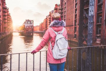 Rear view of adult woman tourist with backpack enjoying sunset on the bridge in Speicherstadt...