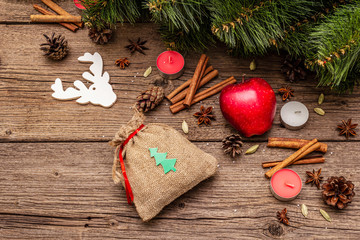 Spirit Christmas background. Gift in sack, New Year tree, apple, candles, spices, deer, cones. Nature decorations, vintage wooden boards