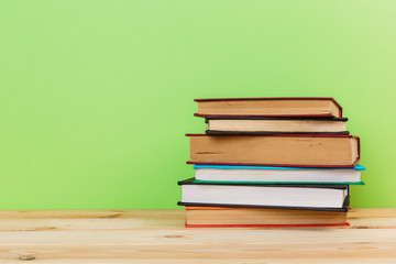 Simple composition of many hardback books, raw of books on wooden table and light green background