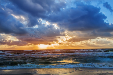 Naklejka na ściany i meble sunset in the cloudy sky over the stormy sea on the sandy shore