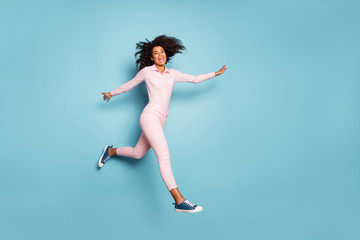 Obraz premium Full length photo of amazing dark skin lady jumping high spread hands sides spending best free time outside wear pink shirt trousers isolated blue color background