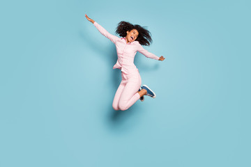 Fototapeta na wymiar Full length photo of amazing dark skin lady jumping high spread hands sides spending best free time wear pink shirt trousers sneakers isolated blue color background
