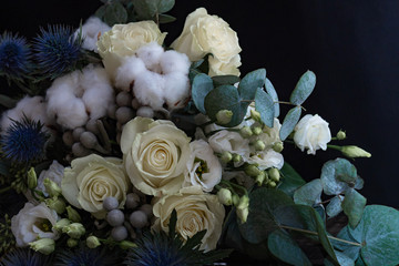 Obraz na płótnie Canvas Winter wedding bouquet of white roses, cotton and eringium on a black background. The bride's bouquet.
