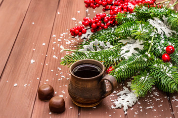 Christmas hot coffee background. New Year fir tree, dog rose, fresh leaves, chocolate candies and artificial snow. Wooden boards backdrop
