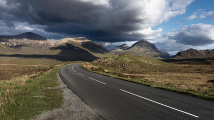 Dramatic sky over country road leading to mountain range in background.Beautiful landscape scene. Road with scenic view.Travel on Isle of Skye, Scotland, UK.