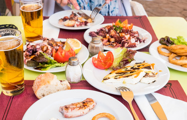 Hands of a Caucasian woman eating an octopus with potatoes made in the Canarian style. Healthy eating. Many dishes on the table. Gold beer