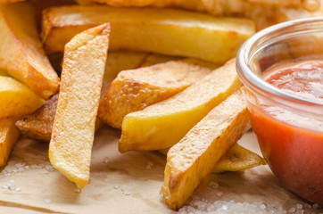 Traditional British street food fish and chips with ketchup sauce on parchment paper