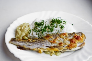 Baked fish with boiled rice and fried onions on a white dish. Healthy diet food.