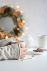 Cozy moment of drinking tea and a Christmas wreath with bokeh lights in the background 