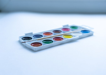 Set of round shaped colorful watercolors in white plastic palette box with tiny brush on white background. Concept of creativity. Art supplies. Selective focus.