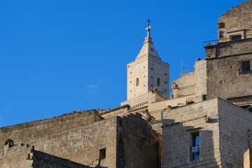 Fototapeta na wymiar Houses and bell tower in the city of Matera in Italy. The tuff blocks are the material used for the construction of the houses.