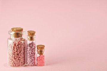 Beige, purple, orange and yellow beads in glass jars on a bright pink background. Beads in a...