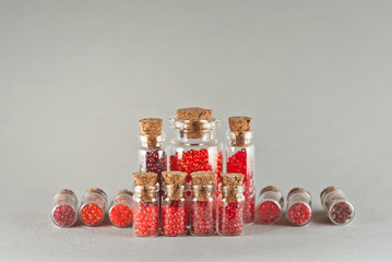 Red and orange beads in glass jars on gray background. Beads in a transparent container with a...