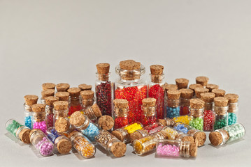 Red, yellow, blue, green, purple, pink and orange beads in glass jars on a gray background. Beads in a transparent container with a wooden cork. The concept of orderliness, balance and chaos.