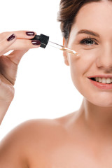 cropped view of happy naked woman holding pipette while applying serum isolated on white