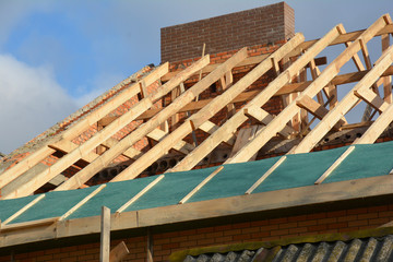 Obraz premium House rooftop wooden frame construction. Incomplete house rooftop roofing construction trusses, vapor barrier, wooden beams, eaves, timber.