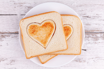 Toasted bread slices with cutted hearts on white plate on wooden table background. Concept of happy family breakfast and Happy Valentine's Day.