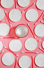 Hygiene products: white round cotton pads and plastic sticks for cleaning the ears lie on a pink background next to face cream