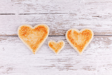 Obraz premium Toasted bread hearts together on white wooden table background. Concept of support in happy family.