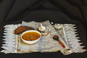 Composition on a homemade linen linen made of pumpkin puree soup, garlic, black bread, pumpkin seeds. Still life.