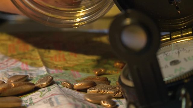 Close-up of male hand holding a glass jar full of gold nuggets. Pouring gold nuggets on a map with a compass on right side. Alberta, Canada. 60fps