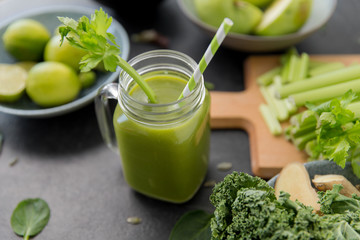 healthy eating, food and vegetarian diet concept - close up of glass mug of fresh green juice or smoothie with paper straw, fruits and vegetables on slate stone background